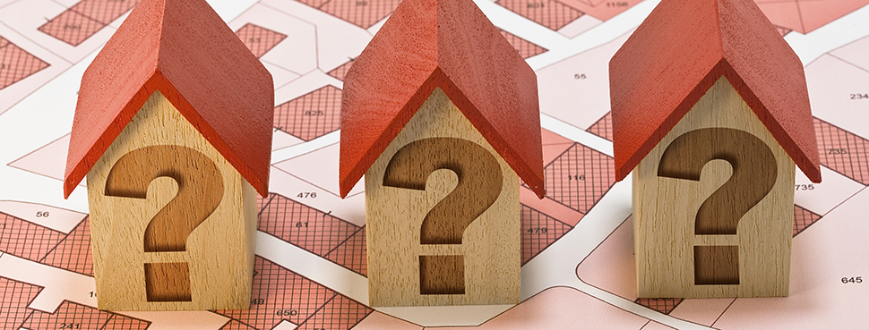 Three toy houses with question marks on their facades sitting on top of a cadastral map.